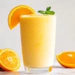 Tall glass of Mango Orange Creamsicle Smoothie with orange slice and mint