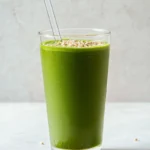 green matcha protein shake in a glass with puffed quinoa and matcha powder on white surface